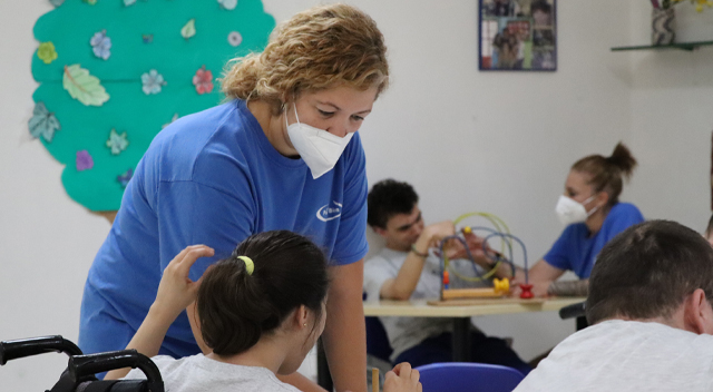 Una trabajadora con mascarilla atendiendo a una persona con discapacidad