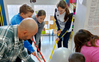 Unos niños jugando con palos y una pelota junto a un adulto