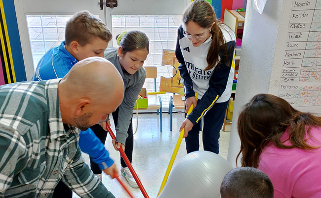 Unos niños jugando con palos y una pelota junto a un adulto