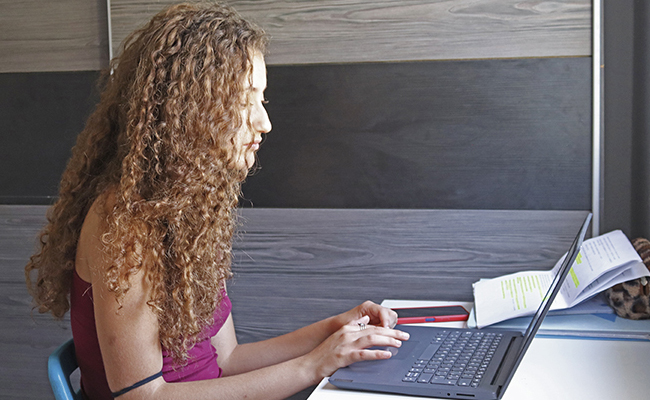 Joven estudiando con un ordenador portátil y documentos. Apoyo educativo para menores del sistema de protección en Sevilla.